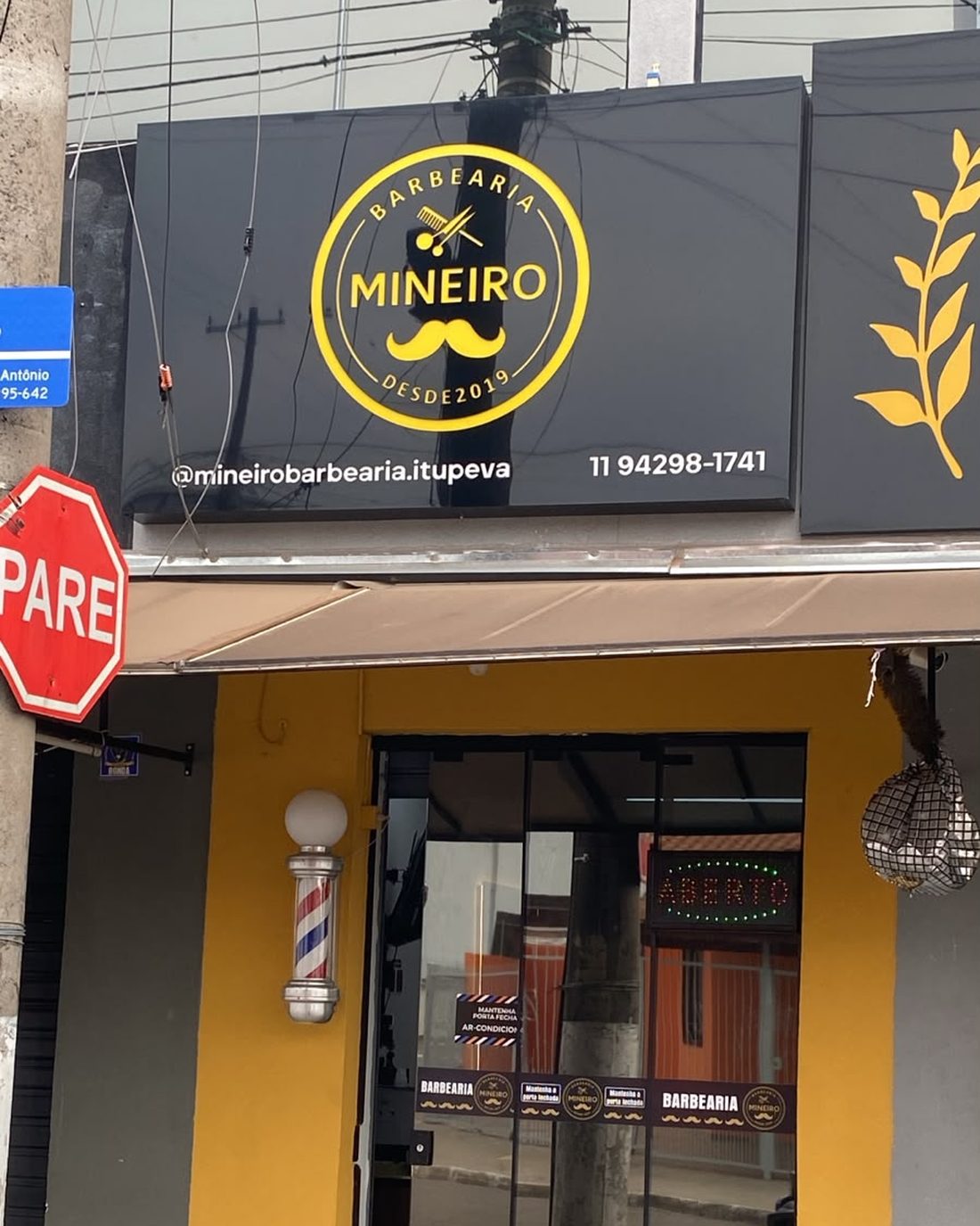 Fachada da Mineiro Barbearia na Rua São Sebastião, em Itupeva, com letreiro preto e dourado e barber pole