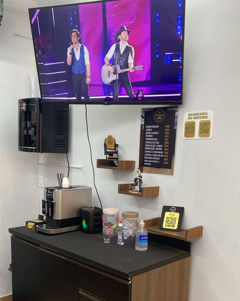 Bancada com cafeteira, TV e cardápio de cafés na Mineiro Barbearia